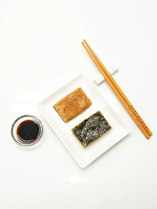 2 Kirimochi de riz brun bio préparé et déposé dans une assiette blanche rectangulaire. L'un des deux est garni d'une feuille de nori. 